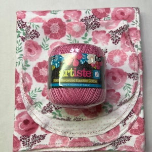 Puede incluir: Una madeja de hilo rosa etiquetada "artiste 100% Mercerized Egyptian Cotton 350 YARD &bull; #10 CROCHET THREAD" sobre un fondo blanco con estampado floral rosa.