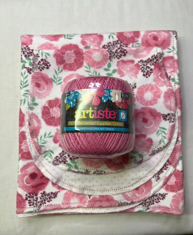 Puede incluir: Una madeja de hilo rosa etiquetada "artiste 100% Mercerized Egyptian Cotton 350 YARD &bull; #10 CROCHET THREAD" sobre un fondo blanco con estampado floral rosa.