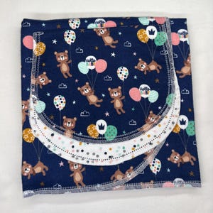 May include: Navy blue baby blanket with a repeating pattern of brown teddy bears holding balloons. The balloons are pink, white, and yellow. The blanket has a white trim with a dotted pattern and the words "Hello Baby".