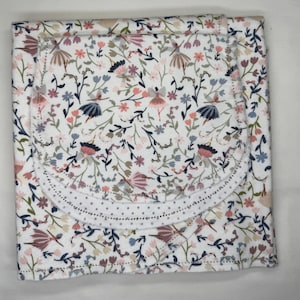 May include: A white baby blanket with a floral and ballerina print. The blanket features a repeating pattern of pink, blue, and brown flowers and ballerinas. The edges are finished with a decorative stitch and a dotted trim.