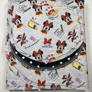 May include: A gray and white fabric with a repeating pattern of Mickey Mouse characters and to-do lists. The fabric is folded in thirds and has a black and white polka dot trim.