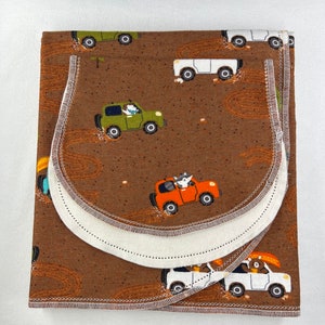 May include: A brown fabric baby burp cloth with a white trim and a repeating pattern of cartoon animals driving cars. The animals include a fox, a bear, and a deer. The cars are all different colors and have different designs.