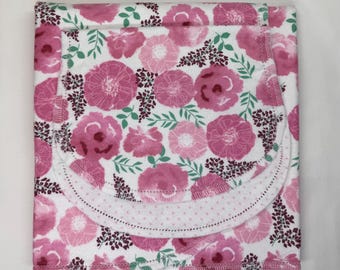 May include: A folded fabric item featuring a white background with a repeating pattern of pink and dark magenta flowers, small green leaves, and dark purple sprigs. The piece includes a curved flap with a light pink and white polka dot border.