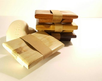 May include: A stack of four wooden soap dishes, each with a different wood grain and color. The top dish is a light brown, the second is a darker brown, the third is a reddish brown, and the bottom dish is a dark brown. The dishes are wrapped with brown paper tape.