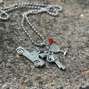 May include: Silver necklace with charms including a car, a gun, a wine glass, and a red bead. The necklace has a ball chain. The charms are detailed and appear to be made of metal.