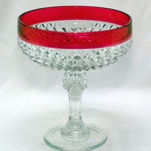 May include: A clear glass pedestal bowl featuring a deep red band around the upper rim. The bowl and the stem are decorated with a faceted diamond-cut pattern. The piece stands on a circular base, showcasing a clear glass construction throughout.
