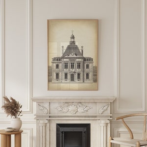 Op de afbeelding: Een zwart-witte tekening van een gebouw met een klokkentoren, ingelijst in een licht houten lijst, hangt boven een witte marmeren open haard met een zwarte haard inzet. De open haard bevindt zich in een kamer met witte muren en lambrisering.