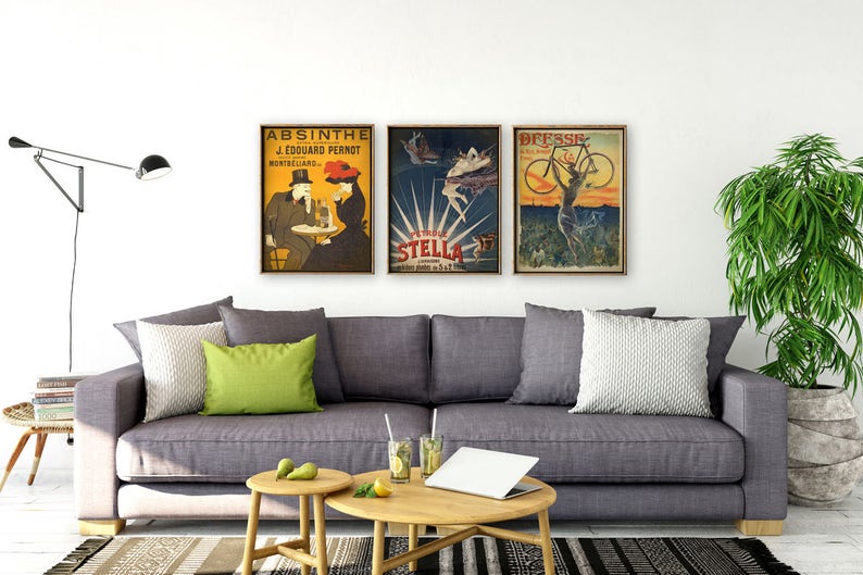 Puede incluir: Tres carteles vintage enmarcados en madera, colgados en una pared blanca sobre un sof&aacute; gris. Los carteles son para Absenta, Stella y Bresse. El sof&aacute; tiene cojines verdes y blancos y un ordenador port&aacute;til sobre una mesa de caf&eacute; de madera delante de &eacute;l.