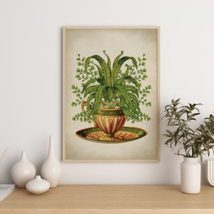 May include: A vintage botanical illustration of a fern plant growing in a teacup and saucer. The teacup is decorated with green and gold accents. The illustration is framed in a light wood frame.