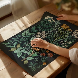 May include: A black background with a botanical illustration of various green leaves and flowers in shades of yellow, white, and orange. The illustration is printed on a flat surface.