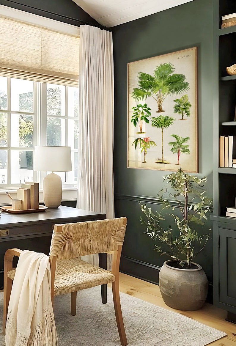 Puede incluir: Una oficina en casa con una pared verde oscuro, una gran impresi&oacute;n bot&aacute;nica enmarcada de palmeras, un escritorio de madera con una l&aacute;mpara, una silla tejida y una planta en maceta en una maceta de terracota.