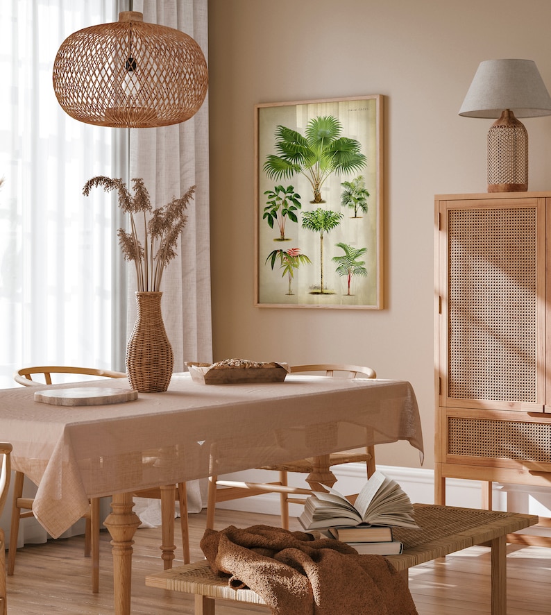Puede incluir: Un comedor con una mesa y sillas de color marr&oacute;n claro, una pantalla de l&aacute;mpara de tejido marr&oacute;n que cuelga del techo, un jarr&oacute;n de tejido marr&oacute;n con hierbas secas de color beige, una impresi&oacute;n bot&aacute;nica enmarcada de palmeras, un armario de tejido marr&oacute;n y una mesa de caf&eacute; de tejido marr&oacute;n con una manta marr&oacute;n y libros.