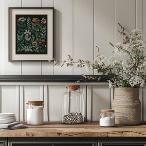 May include: Three glass jars with wooden lids on a wooden worktop. The jars are filled with white powder, white beans, and white powder. A vase with dried white flowers sits on the worktop next to the jars. A framed botanical print hangs on the wall behind the jars.