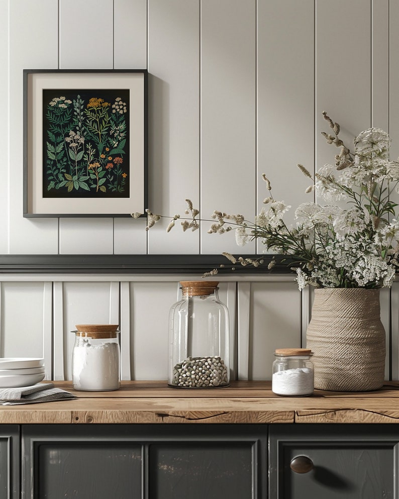 May include: Three glass jars with wooden lids on a wooden worktop. The jars are filled with white powder, white beans, and white powder. A vase with dried white flowers sits on the worktop next to the jars. A framed botanical print hangs on the wall behind the jars.