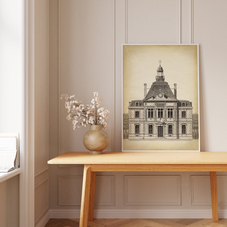 Op de afbeelding: Een zwart-witte lijntekening van een gebouw met een klokkentoren. De tekening is op een beige achtergrond en ingelijst in een wit frame. De tekening hangt aan een muur boven een houten tafel.