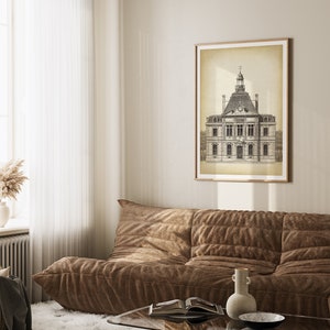 Op de afbeelding: Een zwart-witte illustratie van een gebouw met een klokkentoren, ingelijst in een licht houten lijst en hangend aan een beige muur boven een bruine bank.