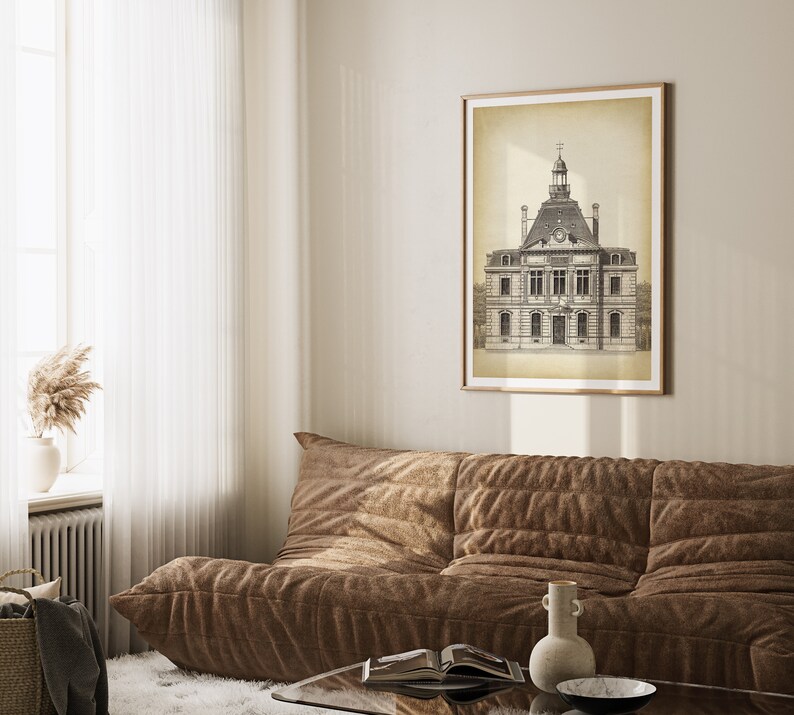 Op de afbeelding: Een zwart-witte illustratie van een gebouw met een klokkentoren, ingelijst in een licht houten lijst en hangend aan een beige muur boven een bruine bank.