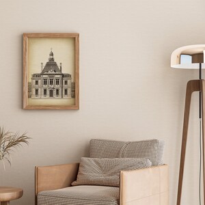 Op de afbeelding: Een ingelijste zwart-witprint van een oud gebouw met een klokkentoren. De print hangt aan een beige muur boven een bruine fauteuil met een geruit patroon. Een hoge houten staande lamp met een zilveren lampenkap staat in de hoek van de kamer.
