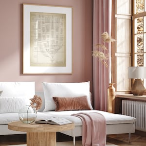 May include: A white couch with a pink throw blanket and a brown throw pillow sits in a room with a pink wall and a framed print of a tree diagram. A wooden coffee table with a book and a vase with dried flowers sits in front of the couch.