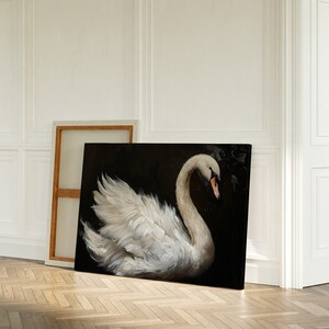 May include: A white swan with its head turned to the side, painted on a black canvas. The swan is in a graceful pose with its wings spread out. The painting is framed and leaning against a white wall.