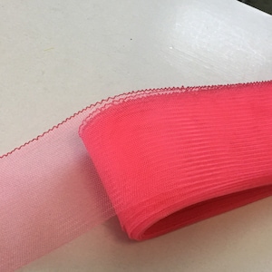 Puede incluir: Un rollo de cinta de tul rosa vibrante con un borde delicado y ondulado. La cinta pasa de un rosa más claro a un tono más brillante y saturado. Esta cinta decorativa es adecuada para manualidades, envolver regalos y decoraciones de eventos.
