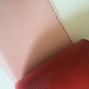 Puede incluir: Dos piezas de tela transparente, una rosa y otra roja, con un tejido texturizado. La tela está doblada, mostrando ambos colores.