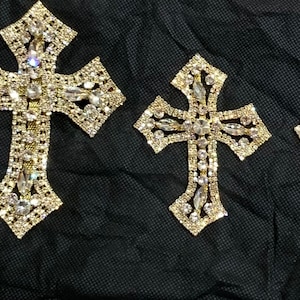 May include: Three gold-toned cross-shaped embellishments with clear rhinestones. The largest cross is approximately 4 inches tall.