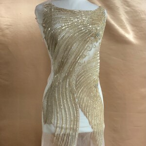 May include: A gold beaded embellishment for clothing or crafts. The embellishment is made of small, shiny beads that are sewn together in a delicate pattern. The embellishment is perfect for adding a touch of sparkle and elegance to any project.