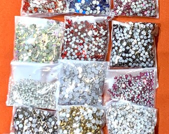May include: Assortment of small, round, clear, and colored rhinestones in individual plastic bags. The rhinestones are in various colors, including silver, gold, red, blue, black, and pink.