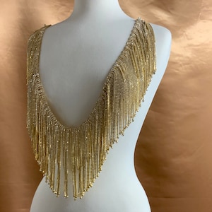 May include: A gold rhinestone fringe trim with a V-neck shape. The fringe is made of small, clear rhinestones that are sewn onto a gold thread.