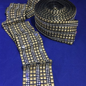 Puede incluir: Un rollo de ribete dorado y negro con filas de diamantes de imitación transparentes. El ribete está hecho de una tela texturizada y tiene un diseño en relieve.