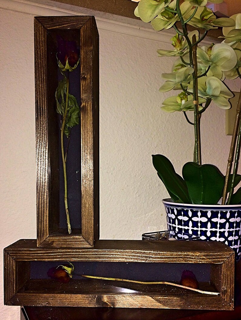 May include: Two wooden shadow boxes with preserved roses. One box is vertical, the other horizontal. The roses are deep red with green leaves, set against a dark blue background. The wood frames have a dark stain.