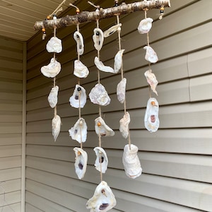 May include: A white oyster shell wind chime with wooden beads hanging from a branch. The chime is made of natural materials and has a rustic look.