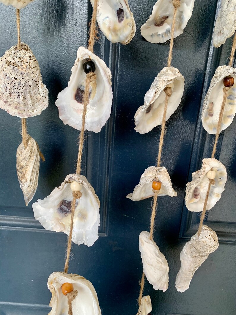 May include: A string of oyster shells with wooden beads hanging from a door. The shells are white and have a natural, organic texture. The beads are brown and add a touch of color to the design.