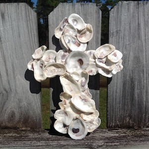 May include: A white cross made of oyster shells, mounted on a wooden fence.