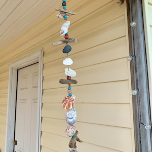 May include: A seashell wind chime with driftwood, turquoise and red beads, and various seashells hanging from a brown twine string.