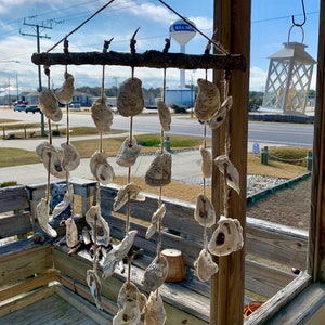 May include: A wooden wind chime with multiple oyster shells hanging from it. The wind chime is hanging from a porch railing with a water tower in the background.