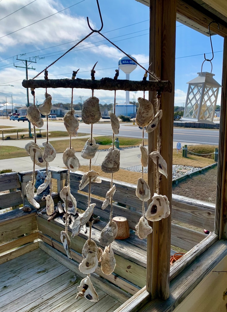 May include: A wooden wind chime with multiple oyster shells hanging from it. The wind chime is hanging from a porch railing with a water tower in the background.