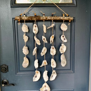 May include: A white oyster shell wind chime hanging from a wooden branch with brown beads. The chime is hanging on a dark blue door.