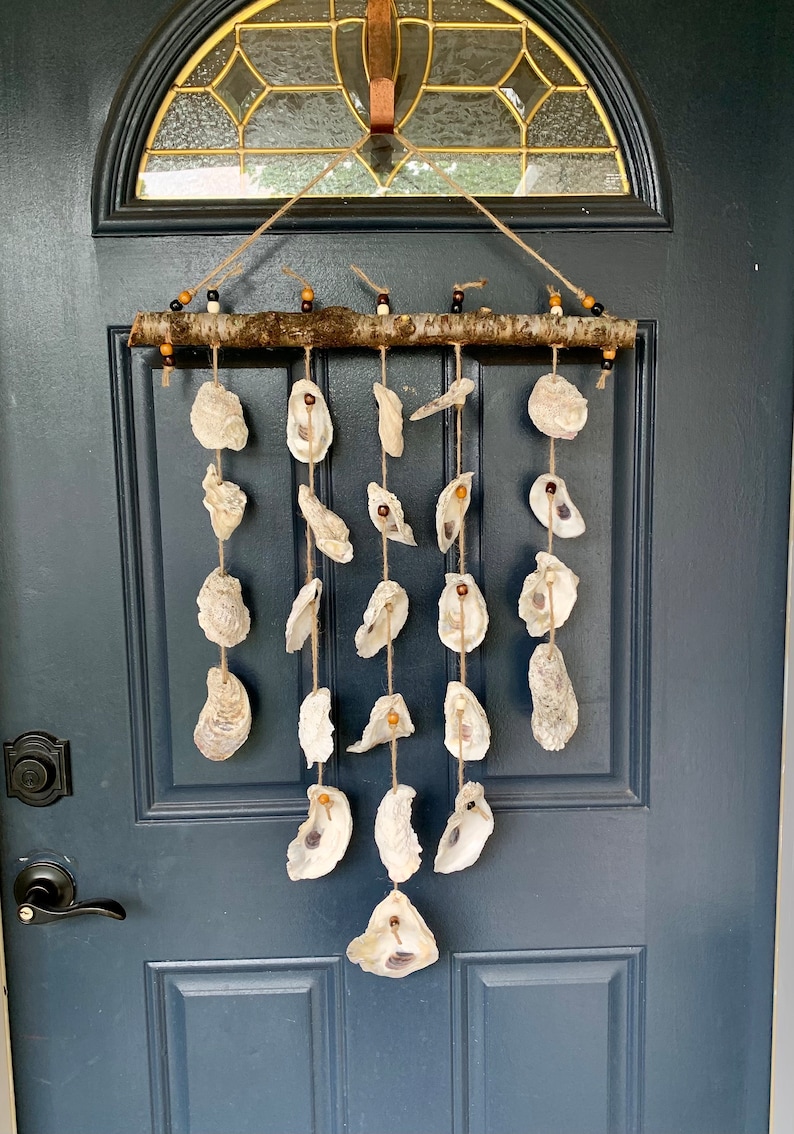 May include: A white oyster shell wind chime hanging from a wooden branch with brown beads. The chime is hanging on a dark blue door.