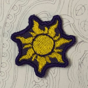 Op de afbeelding: Een geborduurde strijk-op patch met een gestileerde zon in paars en geel.