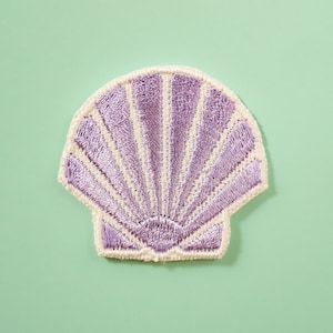Op de afbeelding: Een geborduurde patch in de vorm van een paarse schelp. De patch is perfect om een ​​maritieme of strandlook aan je knutselwerk toe te voegen.