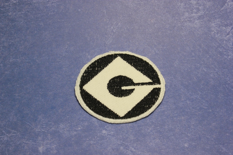 May include: A black and white embroidered patch with the iconic Minion logo, a white G inside a black diamond shape, surrounded by a black circle.