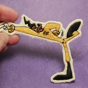 May include: An embroidered iron-on patch featuring a cartoon character in a yellow karate uniform with black hair and a black belt. The character is kicking with their right leg and has a determined expression on their face. The patch has a white background and the word "功夫" is embroidered on the character's chest.