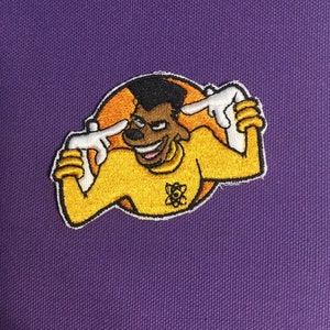 May include: Embroidered patch showing a cartoon character in a yellow shirt with white gloves, pointing at their head. The character is set against an orange circle, with a purple background. The patch includes a science symbol.