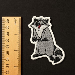 Peut inclure: Patch brodée thermocollante représentant un raton laveur de dessin animé avec une expression espiègle. Le raton laveur est gris avec un ventre blanc et une queue noire. Le patch mesure environ 5 cm de haut.