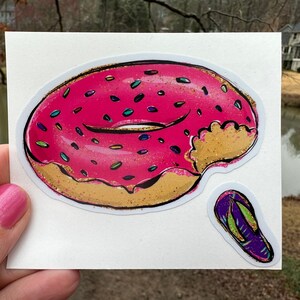 May include: A sticker featuring a pink frosted donut with colorful sprinkles and a bite taken out of it. A small sticker of a purple and green flip-flop is next to the donut. The stickers are on a white background.