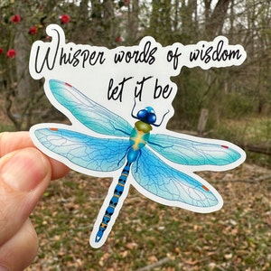 May include: A blue dragonfly with black and yellow markings on its body and wings. The dragonfly is on a white background with the text "Whisper words of wisdom let it be".