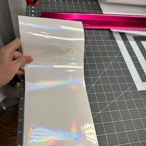May include: A sheet of iridescent vinyl with a rainbow sheen. The vinyl is white with a holographic finish.