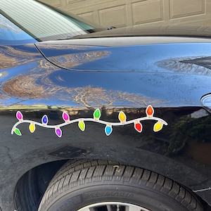 May include: A black car with a string of colorful Christmas lights on the side. The lights are in various colors, including red, green, yellow, blue, and purple.